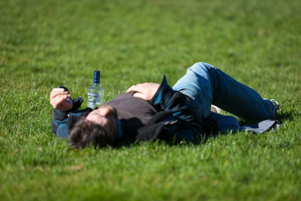 A associação dos bêbados protesta contra o aumento do preço do goró a man laying in the grass with a bottle of beer